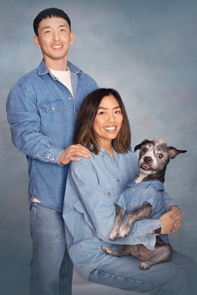 A couple and their dog share a smile, dressed in matching outfits for a fun family photo.