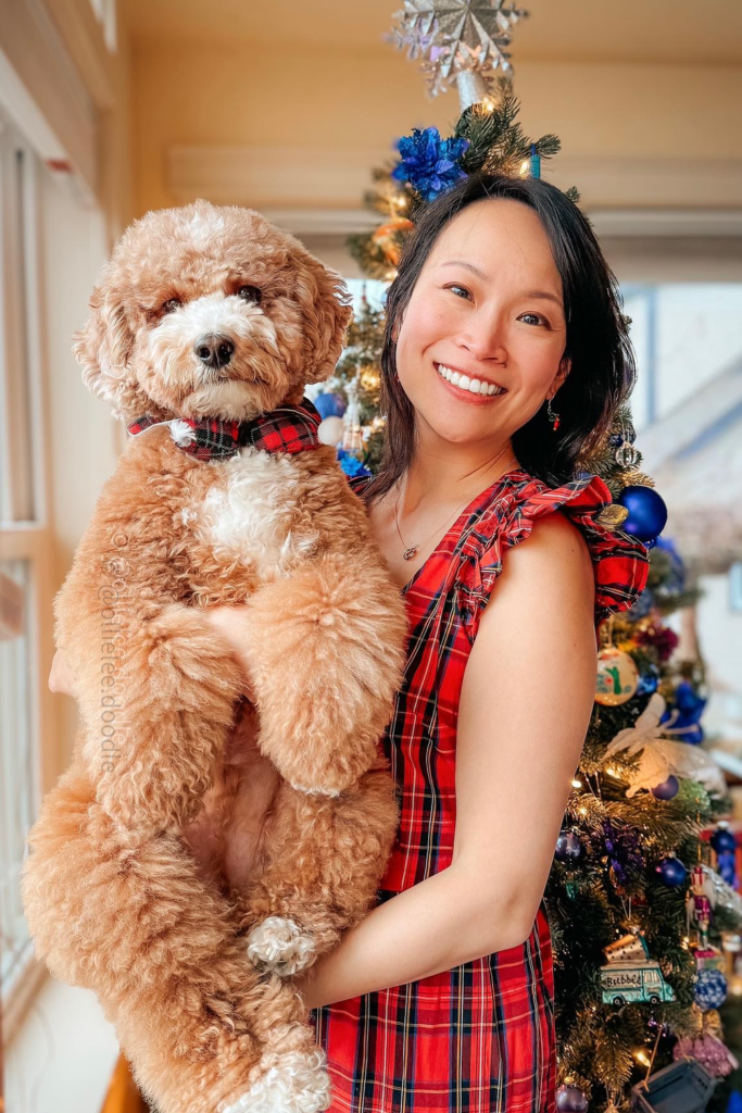Woman in festive Christmas attire smiles for a photo, holding her happy dog.