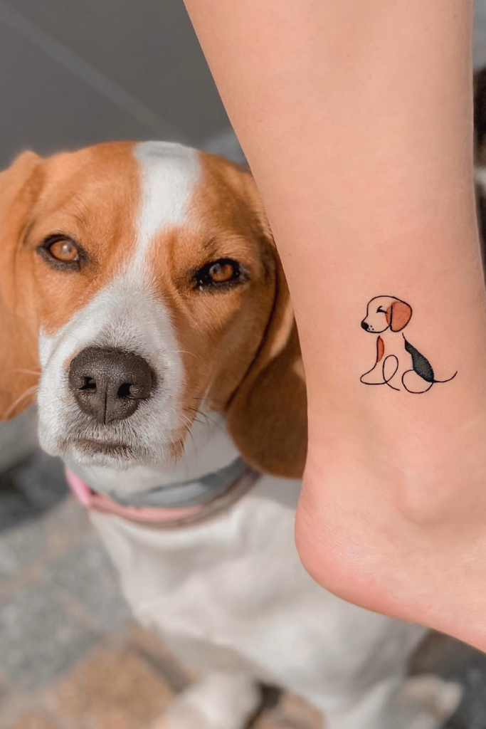 Photo of a Beagle standing next to a person's leg with a tattoo of the dog