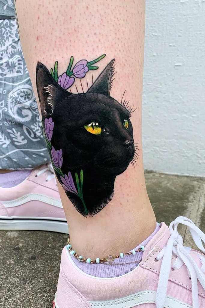 Realistic black cat tattoo on right leg with a single purple flower in full bloom above its head.