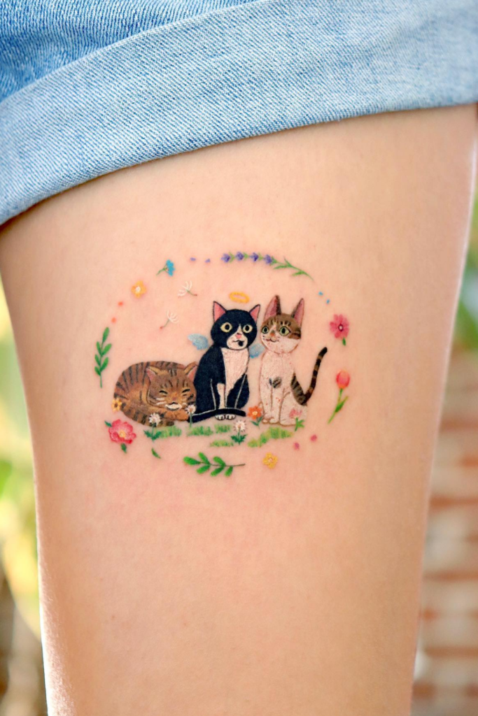 Tattoo of three playful cats drawn in a sketch style, surrounded by a touch of flowers.