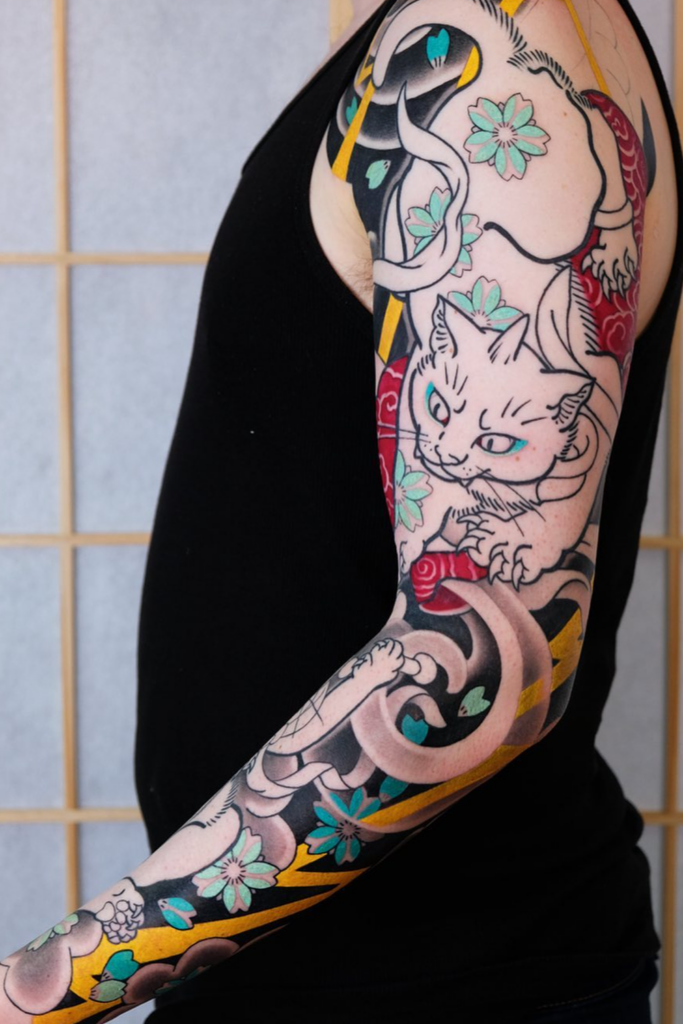 Bold and colorful arm tattoo featuring a cat and stylized flowers in a modern style