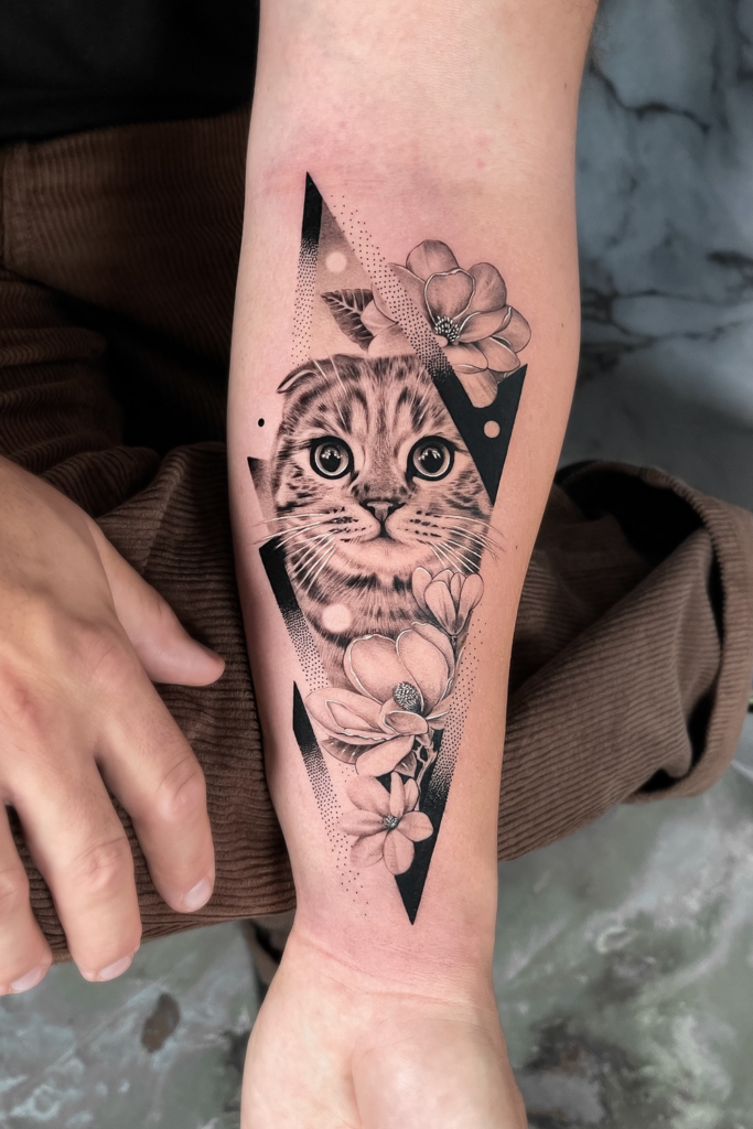 Clear tattoo of a playful cat nestled in blooming flowers on a person's left arm.