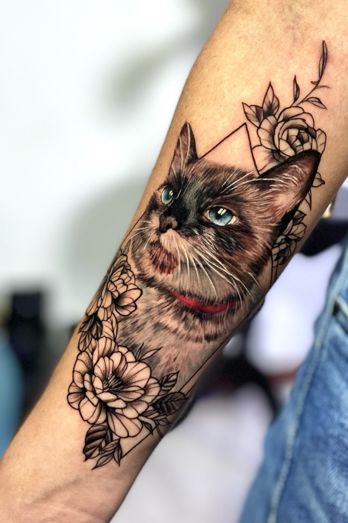 Detailed 3D cat tattoo among delicate flowers, located near a person's elbow.
