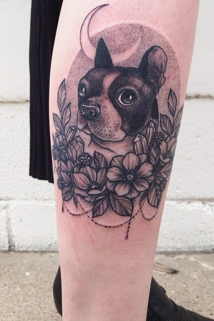Floral dog memorial tattoo on a leg, featuring a dog's portrait tucked within flowers.