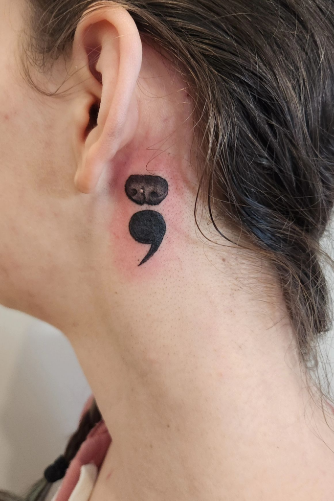 Woman with a dog nose tattoo on the left side of her head, below the ear.