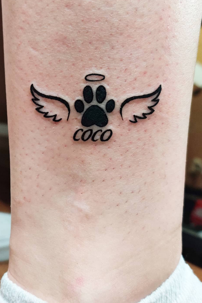 Black paw print dog memorial tattoo with angel wings, remembering 'Coco'