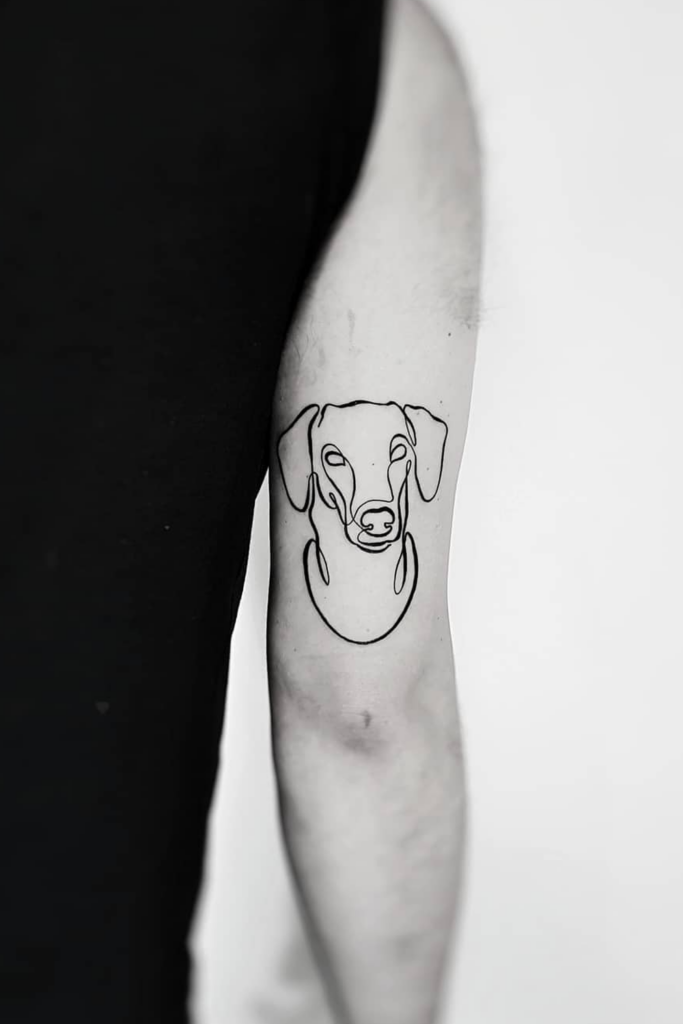 Minimalist dog face tattoo on an elbow, created with simple lines.