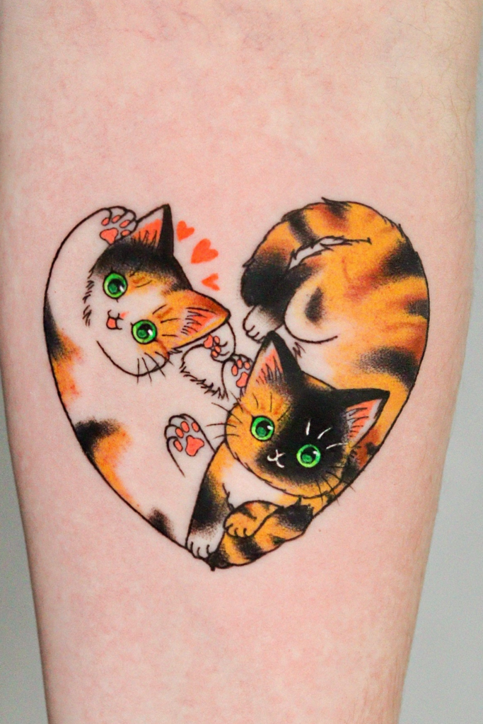Two calico cats curled together in a heart shape on a person's arm tattoo