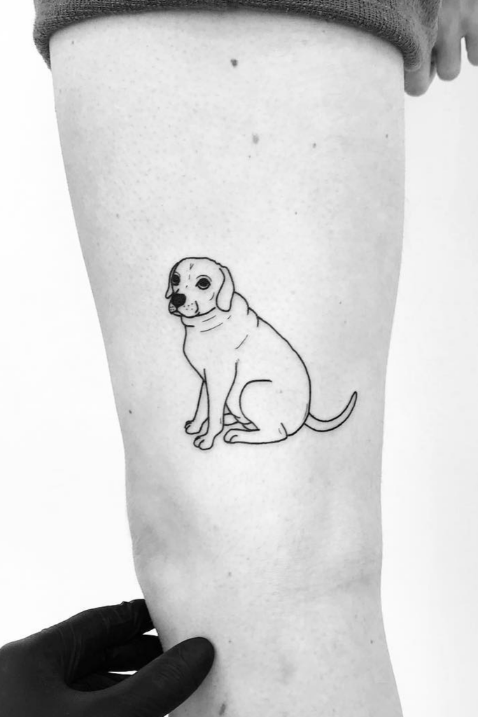 Black and white tattoo of a dog sitting on a leg