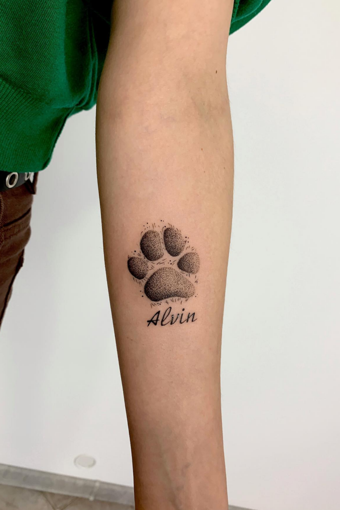A paw printed tattooed arm with name 'Alvin' below the art.