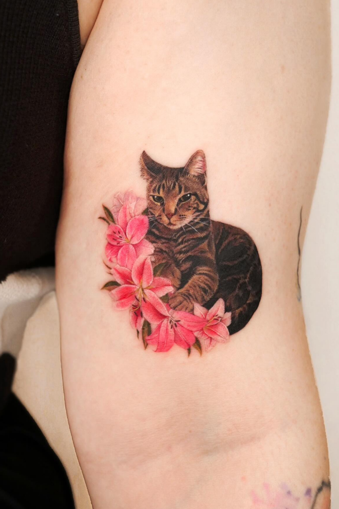 A detailed cat tattoo with vibrant pink flowers blooming around it.