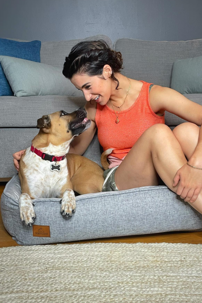 Woman smiles as she embraces her dog on a comfortable dog bed, showcasing their close bond.